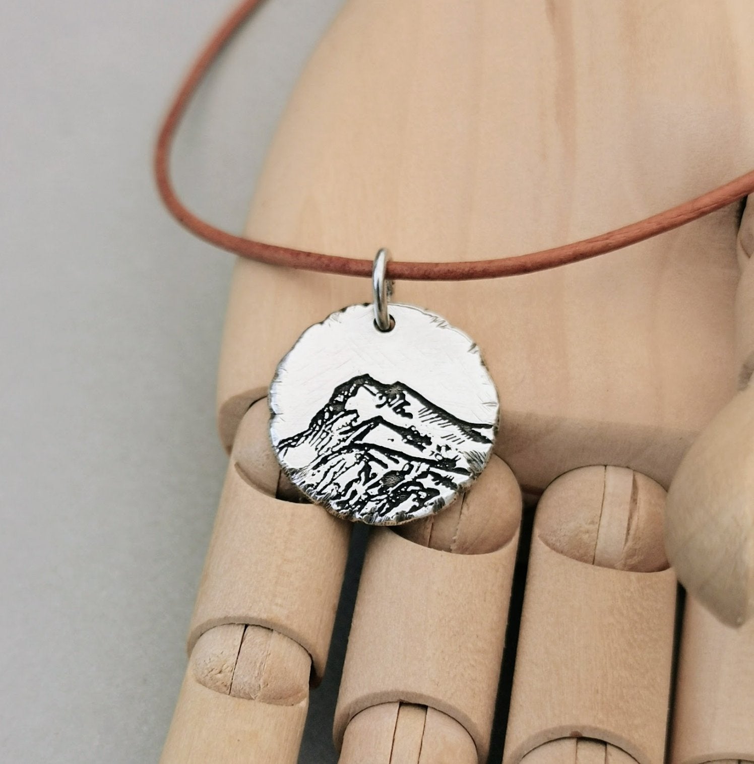 Berg Kette "Der Berg ruft" im Rustic Style, handgefertigt aus recyceltem 925er Silber. Kettenanhänger mit mattem Finish und dunkler Patinierung in den Vertiefungen. Symbolisiert Stärke, Beständigkeit und Naturverbundenheit. Mit oder ohne Kette erhältlich, optional mit individueller Gravur auf der Rückseite. Nachhaltiger Schmuck, hergestellt in Deutschland. Perfekt verpackt, ideal als Geschenk für Wanderer und Skifahrer.