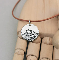 Berg Kette "Der Berg ruft" im Rustic Style, handgefertigt aus recyceltem 925er Silber. Kettenanhänger mit mattem Finish und dunkler Patinierung in den Vertiefungen. Symbolisiert Stärke, Beständigkeit und Naturverbundenheit. Mit oder ohne Kette erhältlich, optional mit individueller Gravur auf der Rückseite. Nachhaltiger Schmuck, hergestellt in Deutschland. Perfekt verpackt, ideal als Geschenk für Wanderer und Skifahrer.