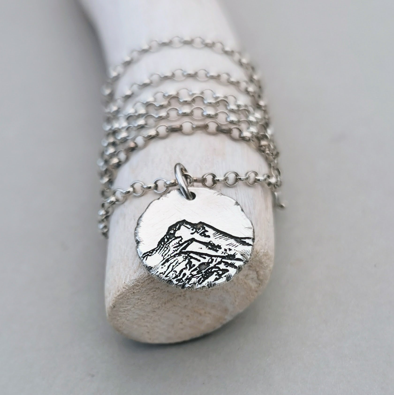 Berg Kette "Der Berg ruft" im Rustic Style, handgefertigt aus recyceltem 925er Silber. Kettenanhänger mit mattem Finish und dunkler Patinierung in den Vertiefungen. Symbolisiert Stärke, Beständigkeit und Naturverbundenheit. Mit oder ohne Kette erhältlich, optional mit individueller Gravur auf der Rückseite. Nachhaltiger Schmuck, hergestellt in Deutschland. Perfekt verpackt, ideal als Geschenk für Wanderer und Skifahrer.