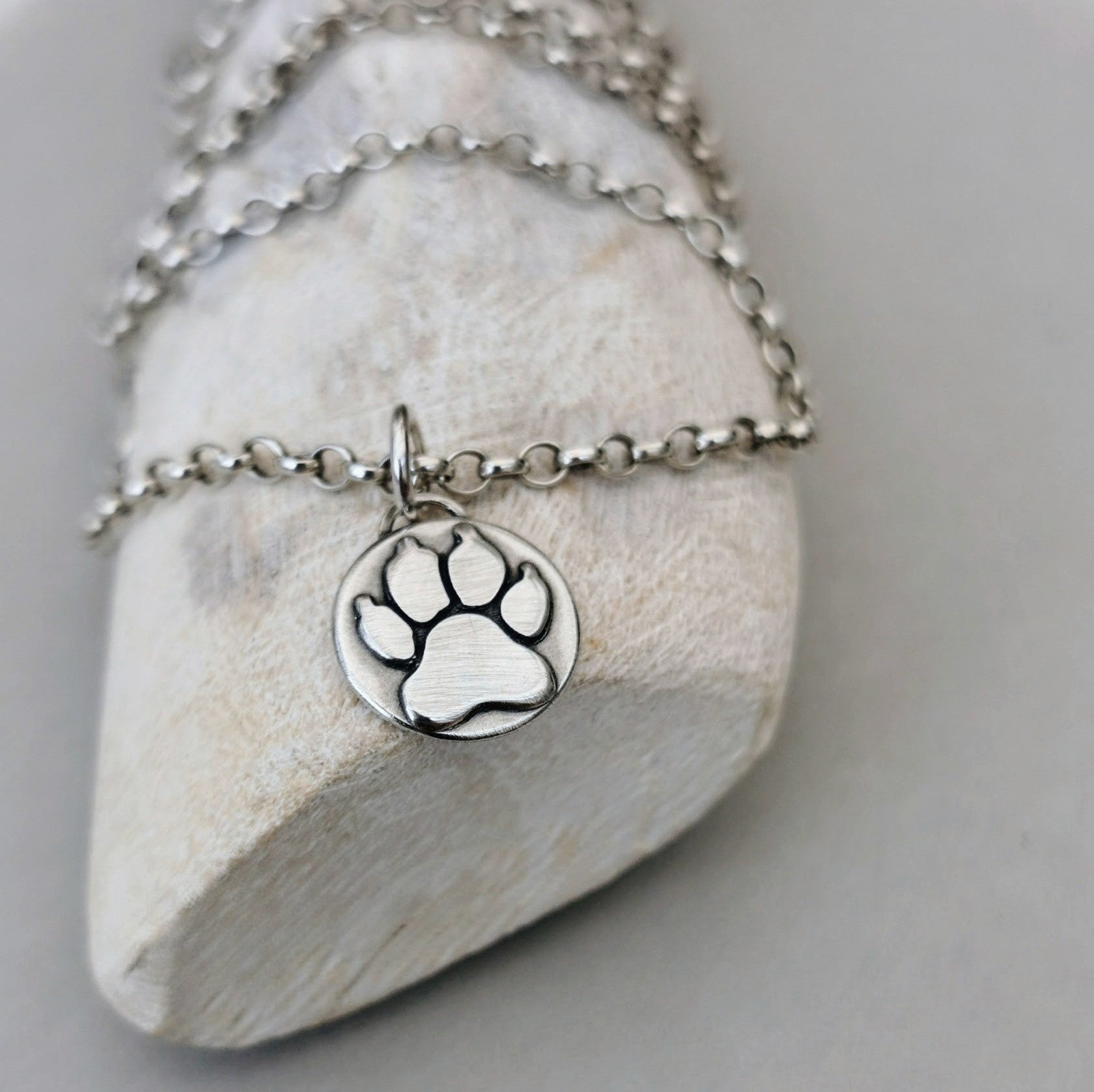 Handgefertigter Kettenanhänger in Form einer Hundepfote aus recyceltem Silber, symbolisiert Liebe und Verbundenheit zu Haustieren, personalisierbar mit Gravur.