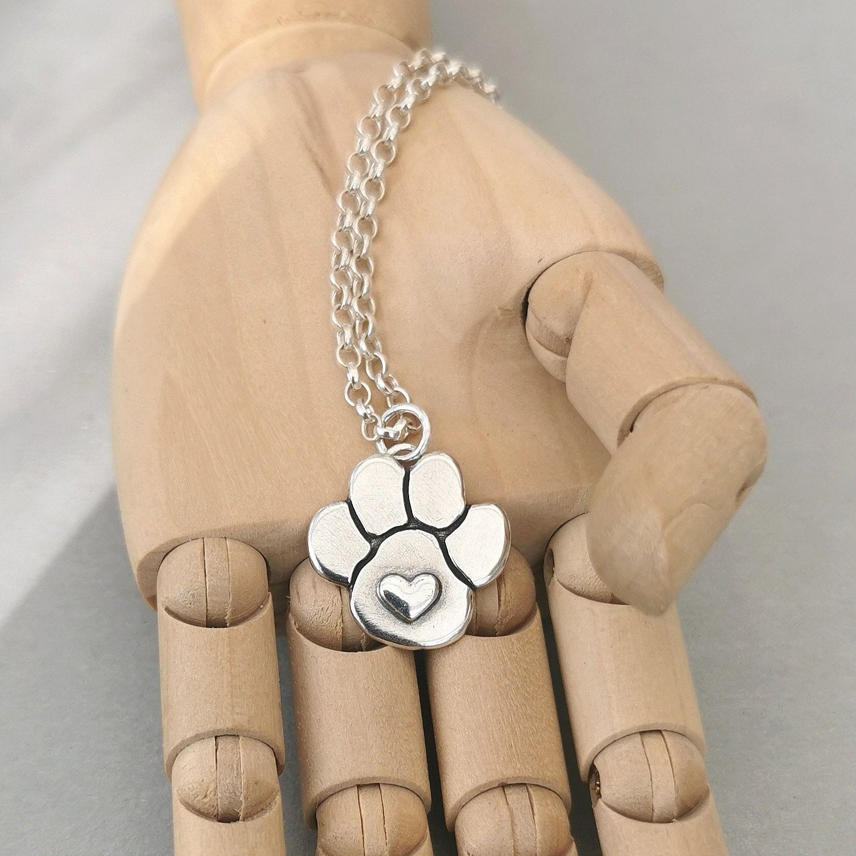 Handgefertigter Kettenanhänger in Form einer Hundepfote mit Herz aus recyceltem Silber, symbolisiert Liebe und Verbundenheit zu Haustieren.