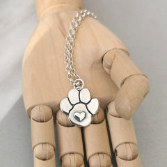 Handgefertigter Kettenanhänger in Form einer Hundepfote mit Herz aus recyceltem Silber, symbolisiert Liebe und Verbundenheit zu Haustieren.