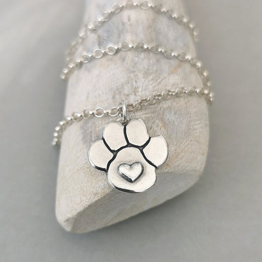Handgefertigter Kettenanhänger aus recyceltem 925er Silber in Form einer Hundepfote mit Herz, Symbol für Liebe zu Haustieren.